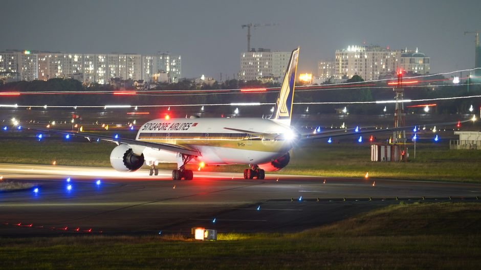 A Singapore Airlines plane on the runway at night amidst city lights and airport lights.