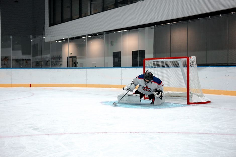 Ice hockey goalie making a save on an indoor rink with safety gear.