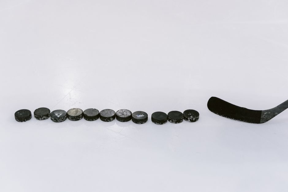 A row of hockey pucks and a stick on an ice rink, perfect for sports content.