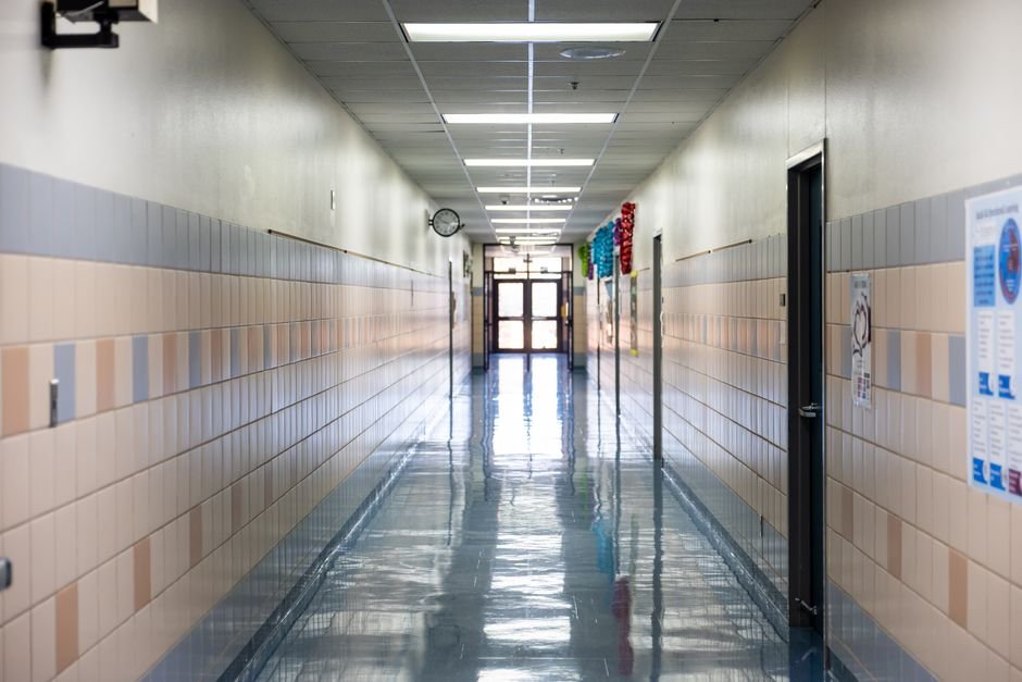 Bright, empty school hallway with fluorescent lighting, reflecting a clean, shiny floor.