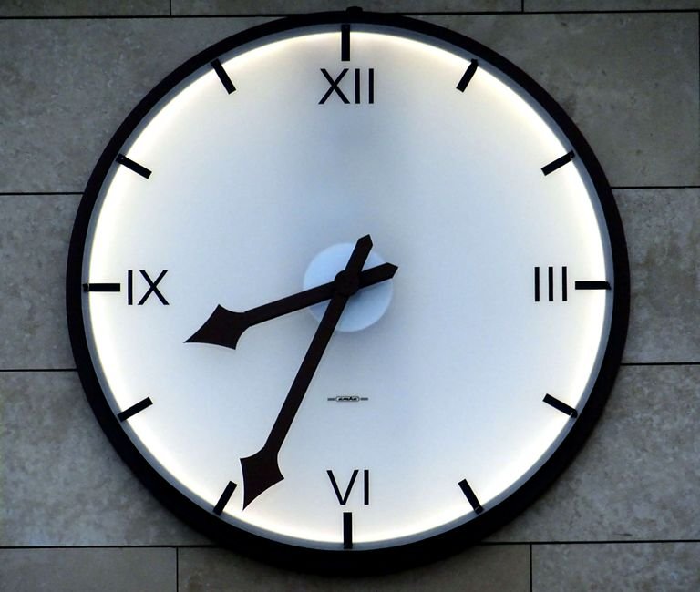 A hand turning an analog clock back one hour as daylight saving time ends in the United States