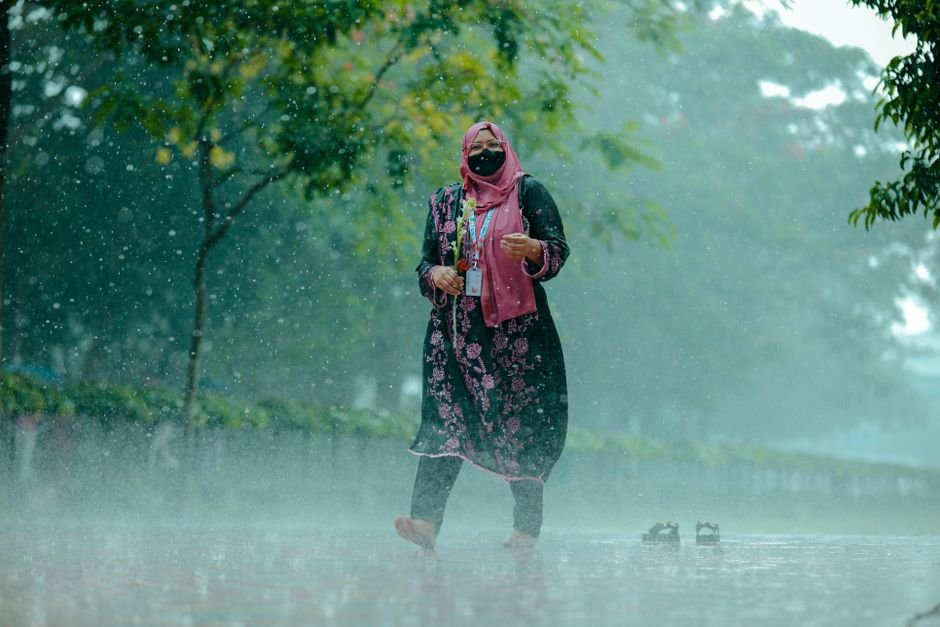 A woman in traditional dress walks barefoot in the rain, embracing the shower.