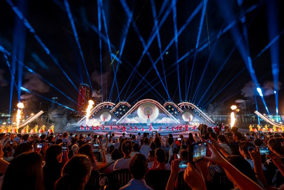 Vibrant nighttime concert featuring a dynamic light show, performers on stage, and a captivated audience capturing moments.